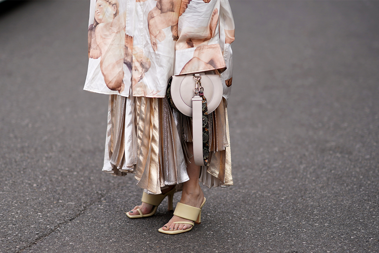 Angela Rozas Saiz wears a large long oversized jacket with long sleeves, a bag with a snake print strap, a pleated dress, cream-color shoes, outside Tod's, during Milan Fashion Week Fall/Winter 2020-2021 on February 21, 2020 in Milan, Italy. 