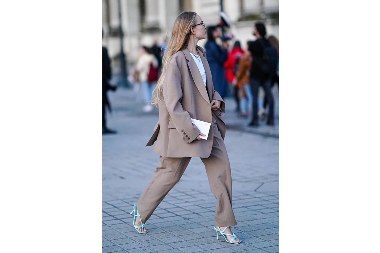 A guest wears earrings, necklaces, a white top, a light brown oversized pantsuit, blue heeled sandals, outside Louis Vuitton, during Paris Fashion Week - Womenswear Spring Summer 2020, on October 01, 2019 in Paris, France. 